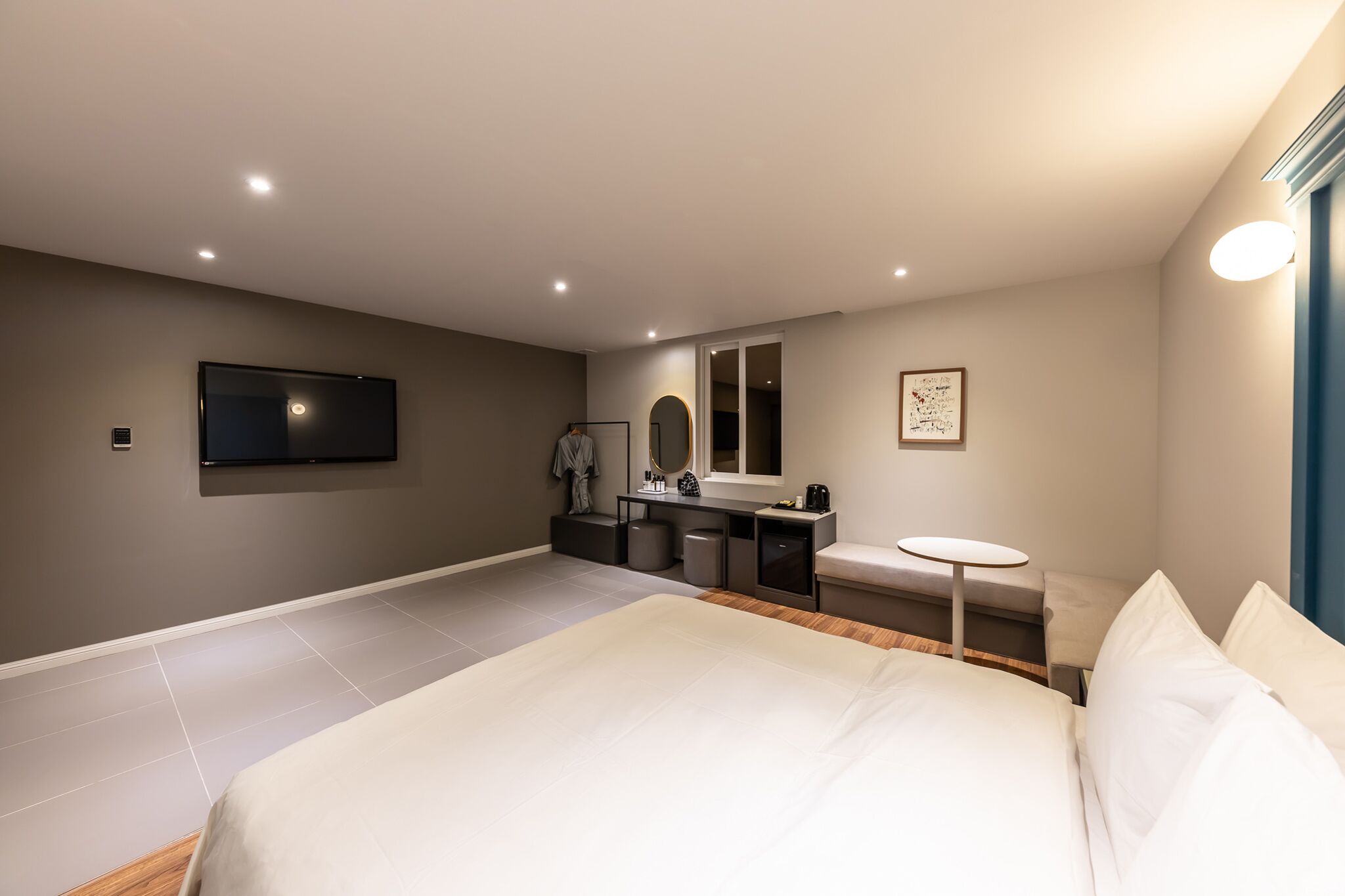 Quarto de hotel moderno com uma cama grande, uma escrivaninha, uma cadeira, uma mesinha e uma televisão fixada na parede, além de um espelho.