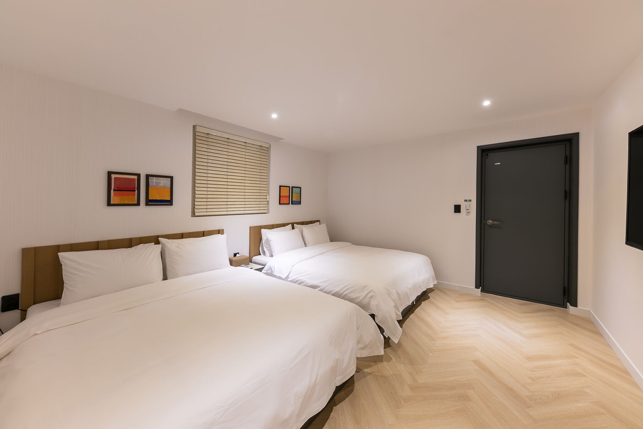 Habitación de hotel con dos camas, una puerta oscura y un suelo de madera clara.