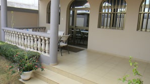 Een overdekt buitengebied met een balkon, een tafel, stoelen en een potplant.