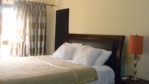 Een hotelkamer met een bed, nachtkastje, lamp, plafondventilator en gordijnen.