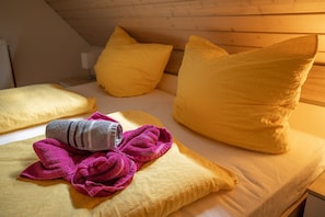 A hotel room with a wooden ceiling, a bed with yellow bedding, and a pink towel on the bed.