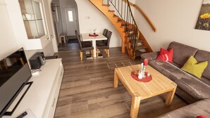 Ein modernes Wohnzimmer mit einer Holztreppe, einem Essbereich und einer Couch mit Kissen.