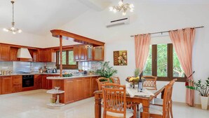 Een ruime keuken met houten kastjes, een centraal eiland en een eetgedeelte met houten stoelen.
