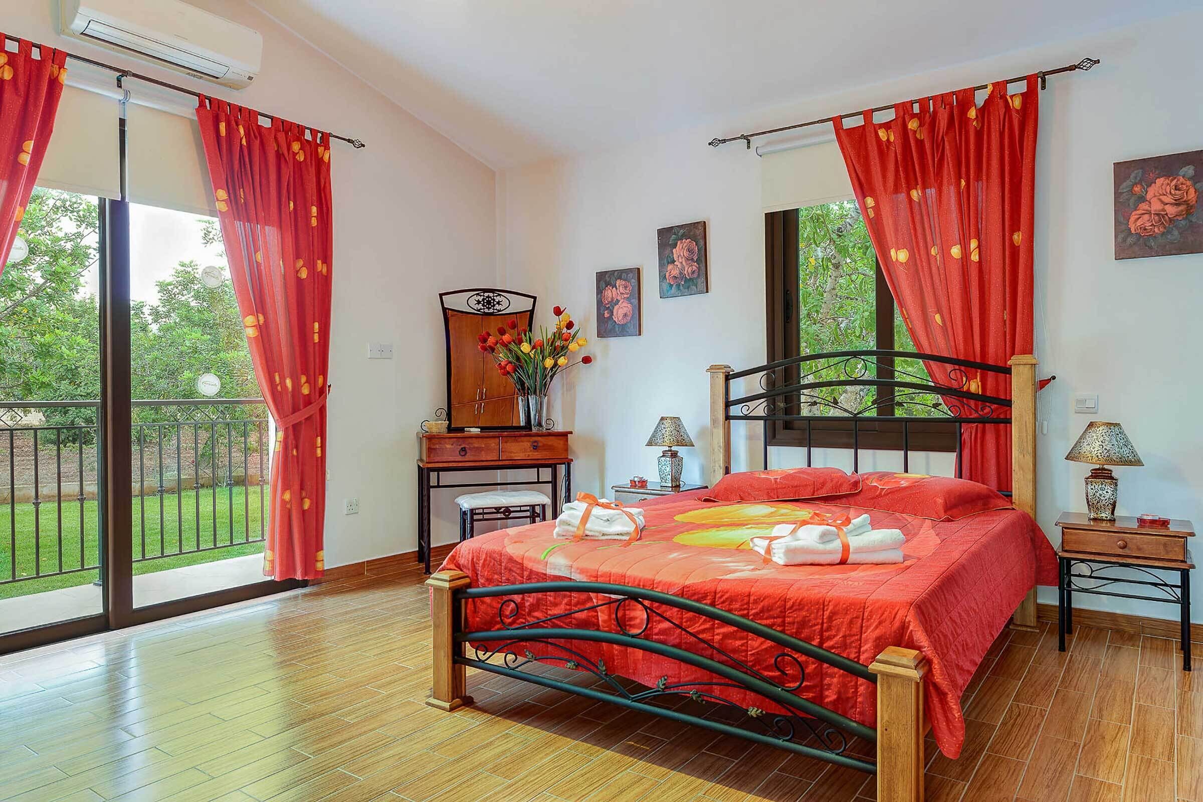 A bedroom with a bed, a desk, a chair, a mirror, and a balcony with red curtains.