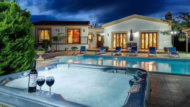 Een zwembad met ligbedden en een jacuzzi, omringd door een goed verlicht terras.
