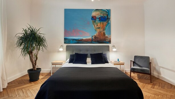 A modern bedroom with a large bed, a potted plant, a chair, and a painting on the wall. - Smart Casual Riga Center Apartment (Centra rajons)