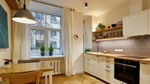 A modern kitchen with a wooden herringbone floor, white cabinetry, a built-in oven, and a window with potted plants. - Smart Casual Riga Center Apartment (Centra rajons)