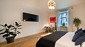 A modern bedroom with a bed, a desk, a potted plant, and a painting. - Smart Casual Riga Center Apartment (Centra rajons)