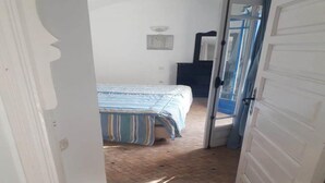 Een smalle gang die uitkomt in een slaapkamer met een bed, een ladekast en een spiegel.