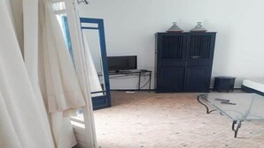 Een kamer met betegelde vloer, een televisie, een donker kastje en een glazen tafel.