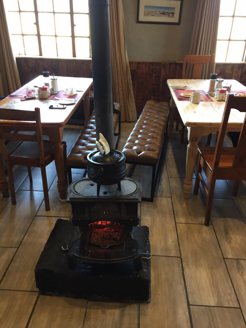 Une pièce équipée d’un poêle à bois, de bancs en bois et de tables avec des chaises.