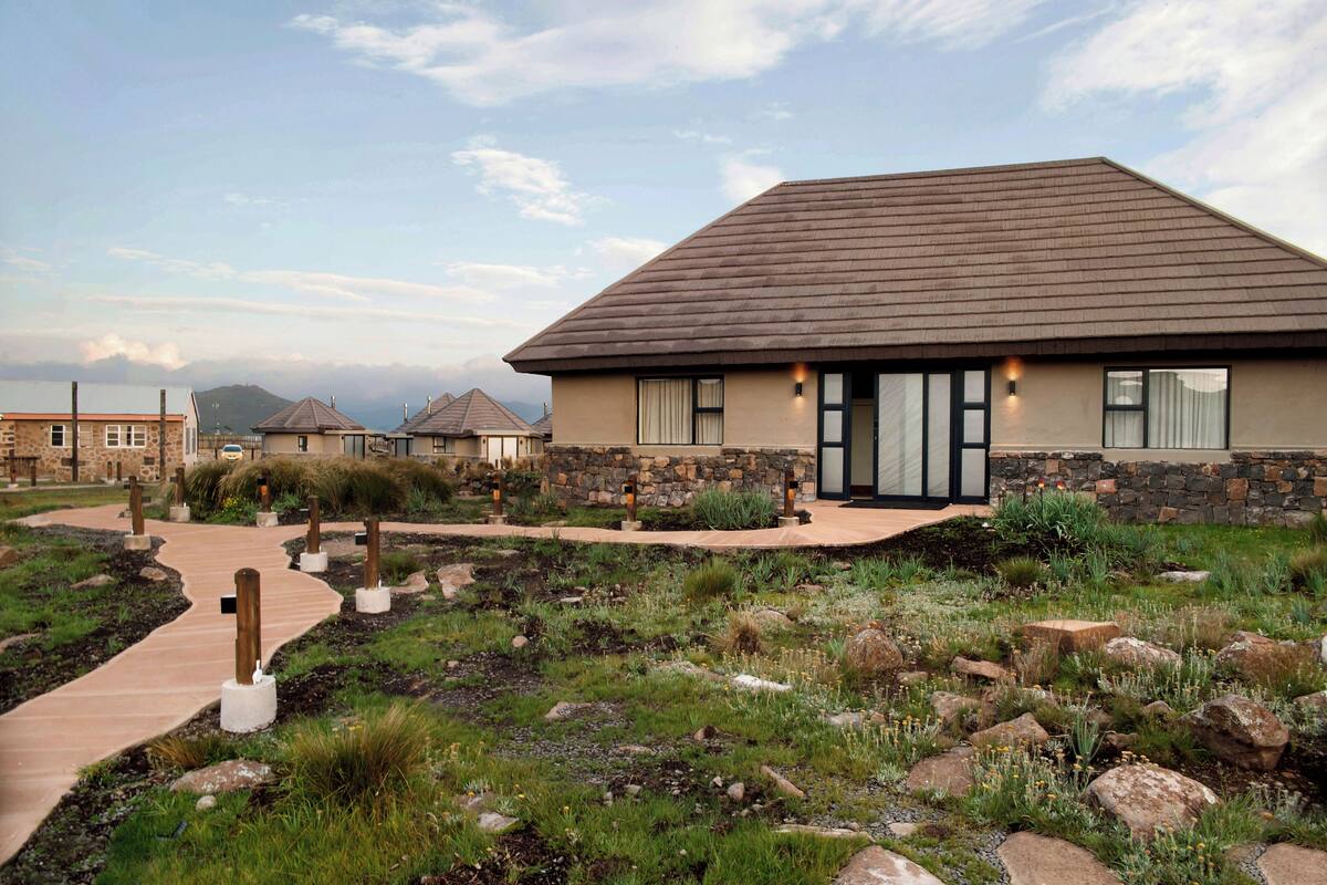 A building with a stone facade, a paved walkway, and a landscaped garden with rocks and plants.