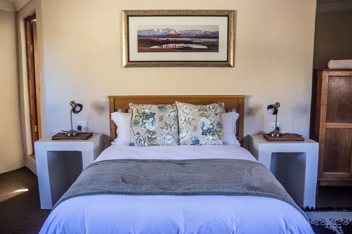 A neatly arranged hotel room with a large bed, two bedside tables with lamps, a framed picture on the wall, and a wooden cabinet.