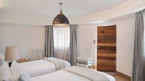A hotel room with two beds, a lamp, a chair, a wooden door, and a hanging light fixture. - Sani Mountain Lodge (Sani Pass)