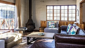 A cozy living room with a fireplace, comfortable seating, and a large window overlooking a scenic view. - Sani Mountain Lodge (Sani Pass)