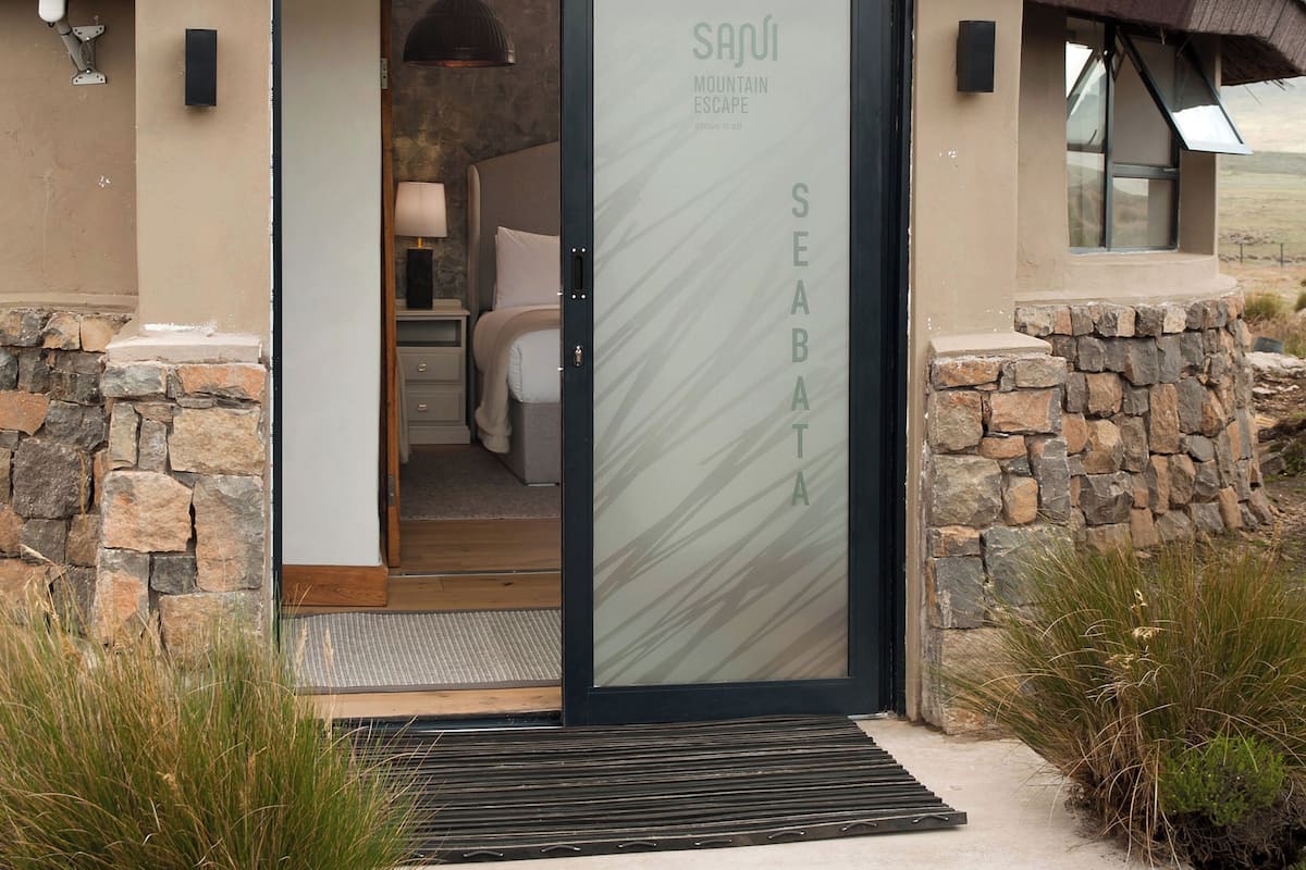A modern building with a stone exterior, a glass door with 'SANJU' and 'SEABAT' signage, and a view of the interior bedroom.