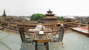 Vista elevada de un edificio tradicional con techo al estilo pagoda, rodeado por una barandilla. En primer plano, hay dos sillas y una mesa.
