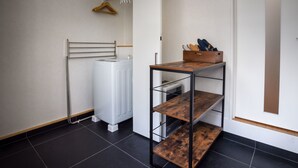 Un rincón de una habitación con un radiador, una estantería metálica y una caja de madera en el suelo.