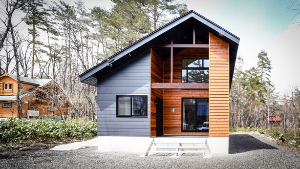 Una casa moderna de dos pisos con fachada gris y detalles de madera, rodeada de árboles.