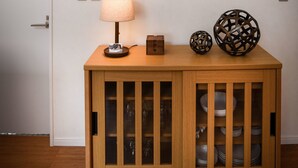 Un aparador de madera con puertas de cristal, una obra de arte de madera montada en la pared, una lámpara de mesa y objetos decorativos.