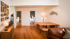 Una habitación de hotel moderna con suelo de madera, una mesa de comedor, un sofá de cuero y una cama con ropa blanca.