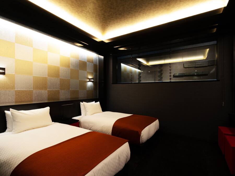 Ein Hotelzimmer mit zwei Betten, einer karierten Wand, einem großen Fenster und einer roten Akzentwand.
