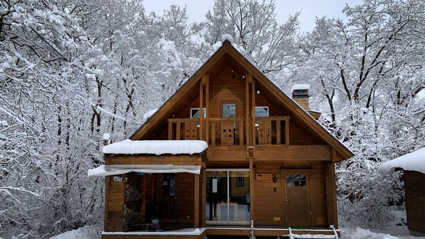 Een houten chalet met balkon, omringd door met sneeuw bedekte bomen.