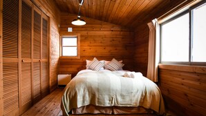A wooden cabin bedroom with a bed, pillows, a window, and a ceiling light. - BETSUINN (Hakuba)