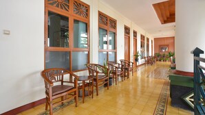 A hallway with wooden chairs and tables, large windows with intricate designs, and a tiled floor. - Kotagede Heritage Homestay (Yogyakarta)