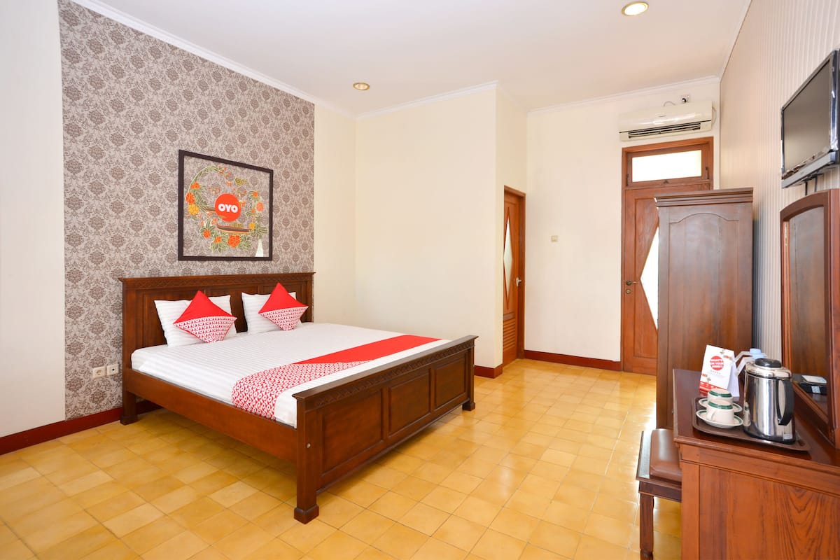 Habitación de hotel con cama de madera, un cuadro enmarcado en la pared, un mueble de madera con cafetera y una puerta que da a otra habitación.
