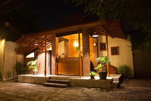 A cozy, well-lit building with a wooden porch, potted plants, and a visible door.