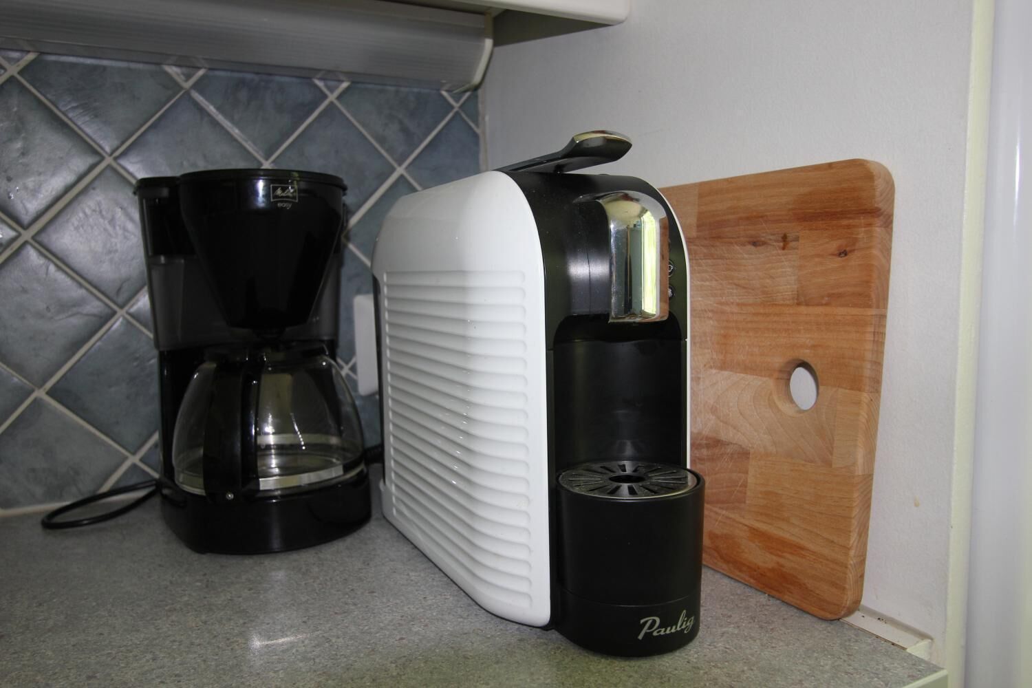 Une cuisine équipée d’une machine à café, d’un distributeur d’eau et d’une planche à découper en bois.