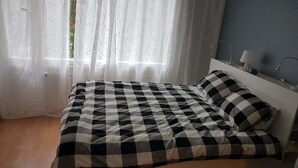 En seng med et ternet sengetæppe, en pude og et natbord med en lampe.