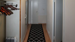 En smal gang med et mønstret tæppe, en radiator og et knagered med hængende ting.