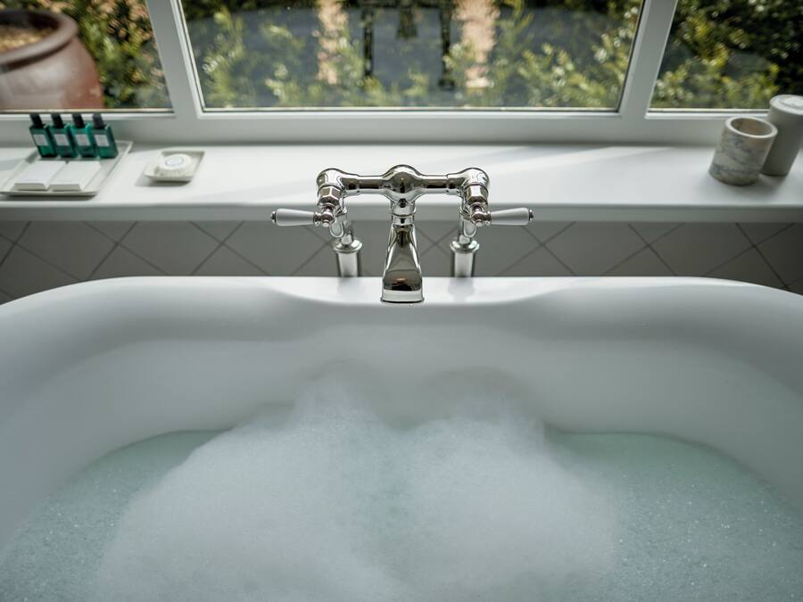 A bathroom with a bathtub, a window, and a shelf with toiletries.