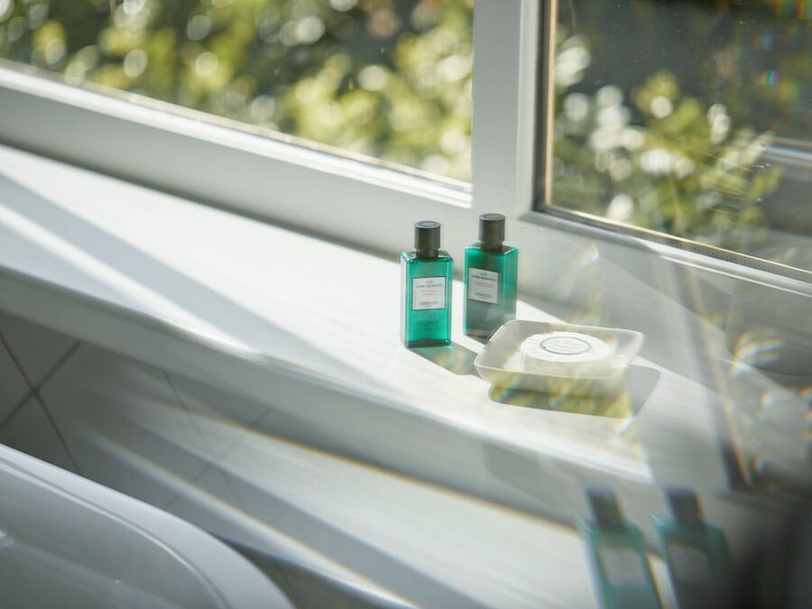 Un baño con ventana, un lavamanos blanco y dos botellas de líquido en el alféizar.