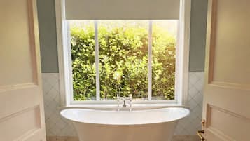 A bathroom with a freestanding bathtub, a window with a view of greenery, and a tiled floor.