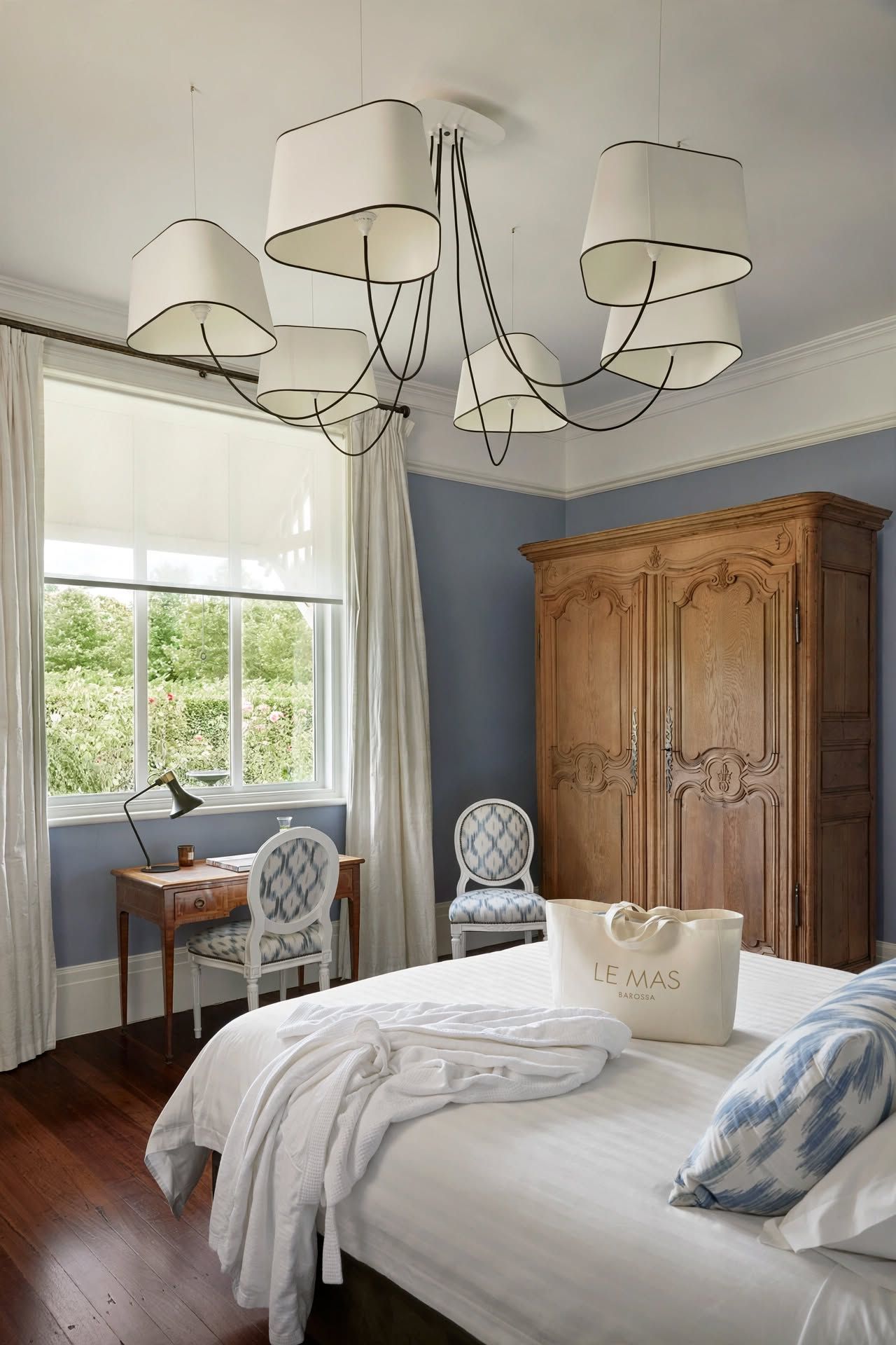 A bedroom with a large bed, a wooden wardrobe, a desk with a chair, and a window with curtains.