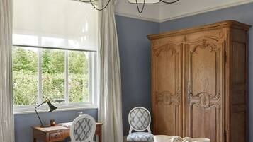 A bedroom with a large bed, a wooden wardrobe, a desk with a chair, and a window with curtains.