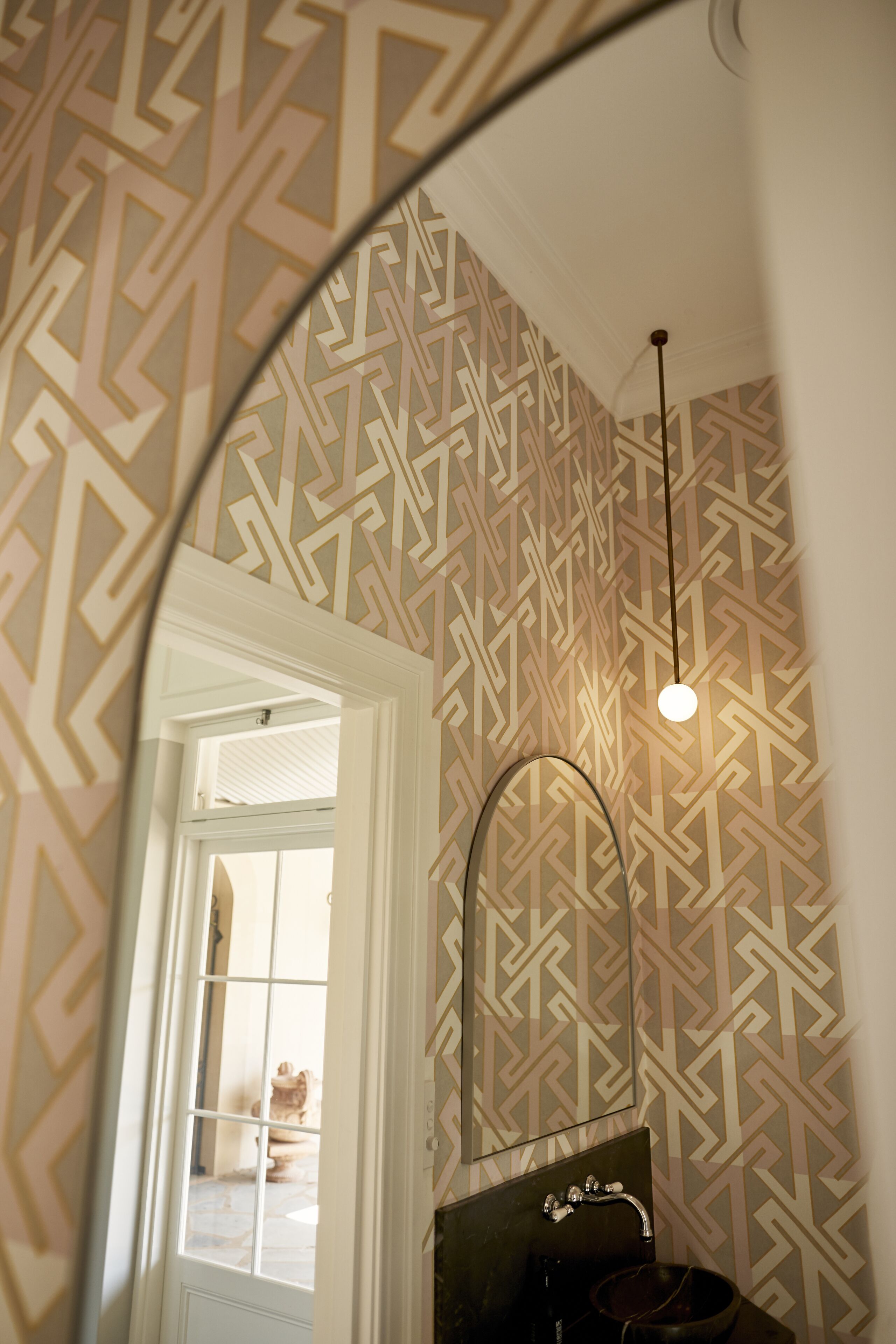 Ein Badezimmer mit einer Wand mit geometrischem Muster, einem Spiegel, einem Waschbecken und einer Pendelleuchte.