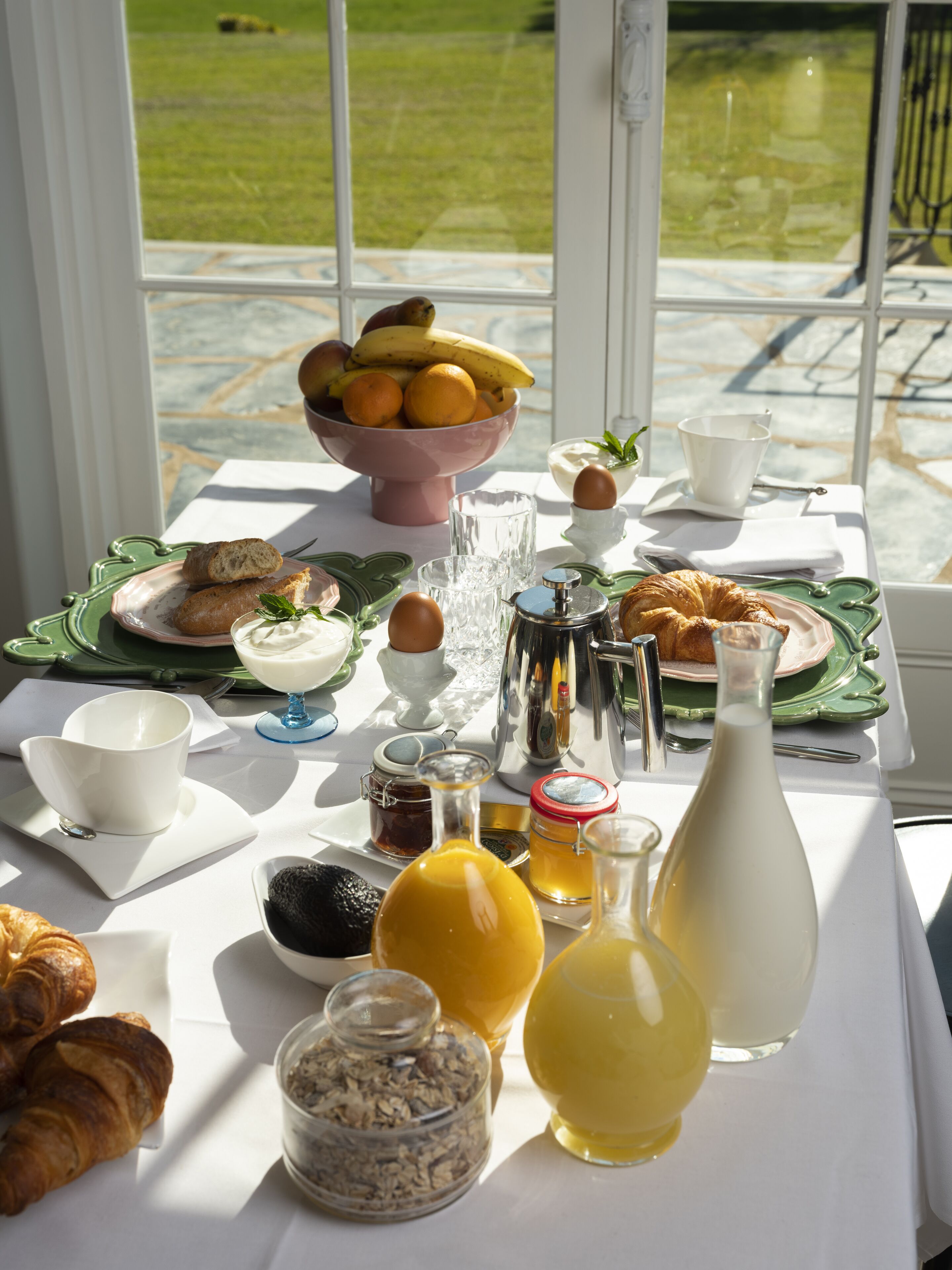 Una mesa de desayuno con croissants, un cuenco de fruta y diferentes condimentos.