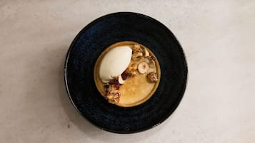 A dessert on a dark plate with a creamy topping and caramelized fruit pieces.