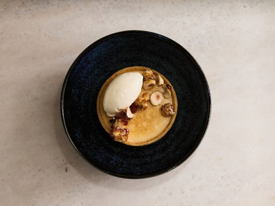 A dessert on a dark plate with a creamy topping and caramelized fruit pieces.