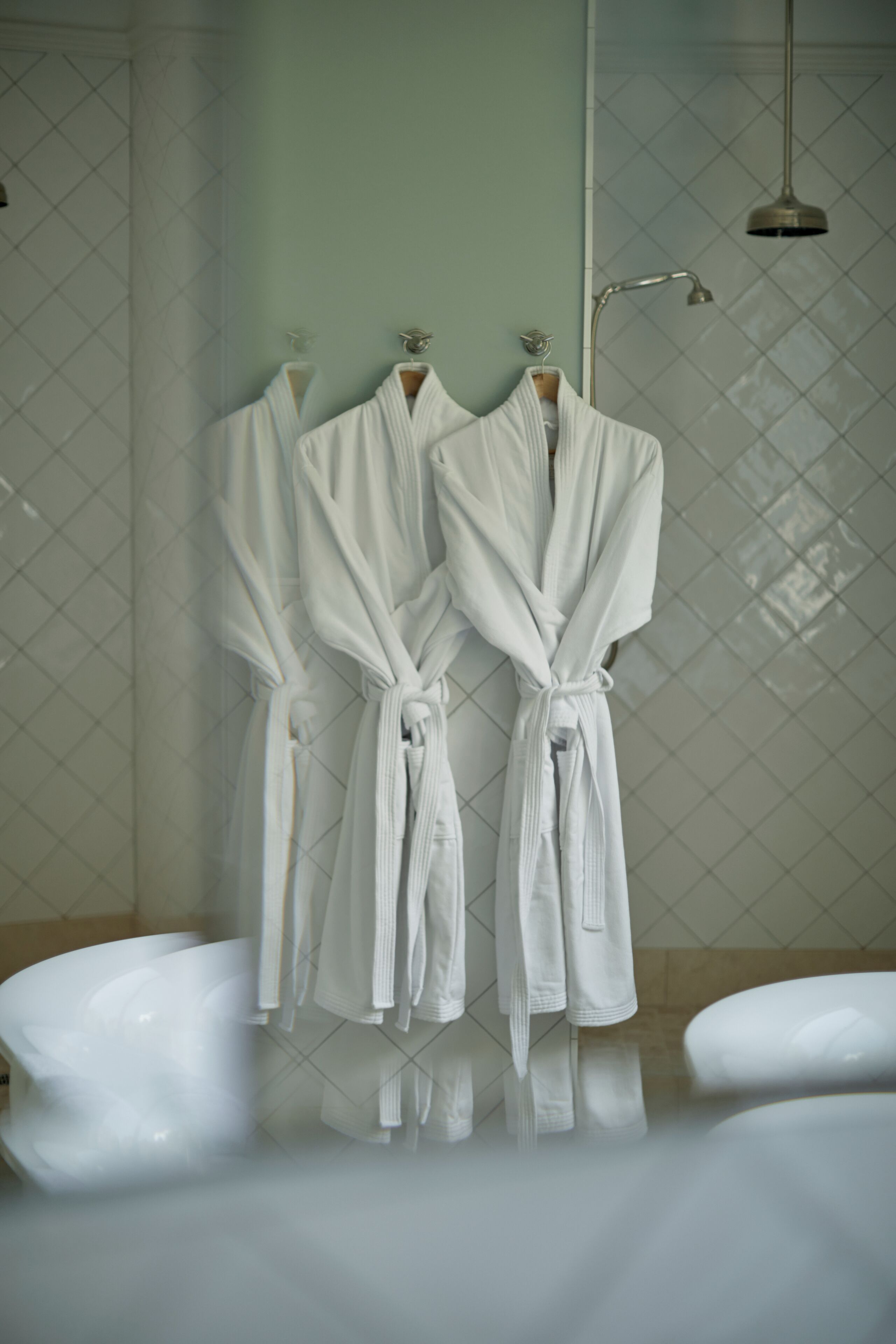 Un baño con tres albornoces blancos colgados en un perchero, un cabezal de ducha y una bañera.