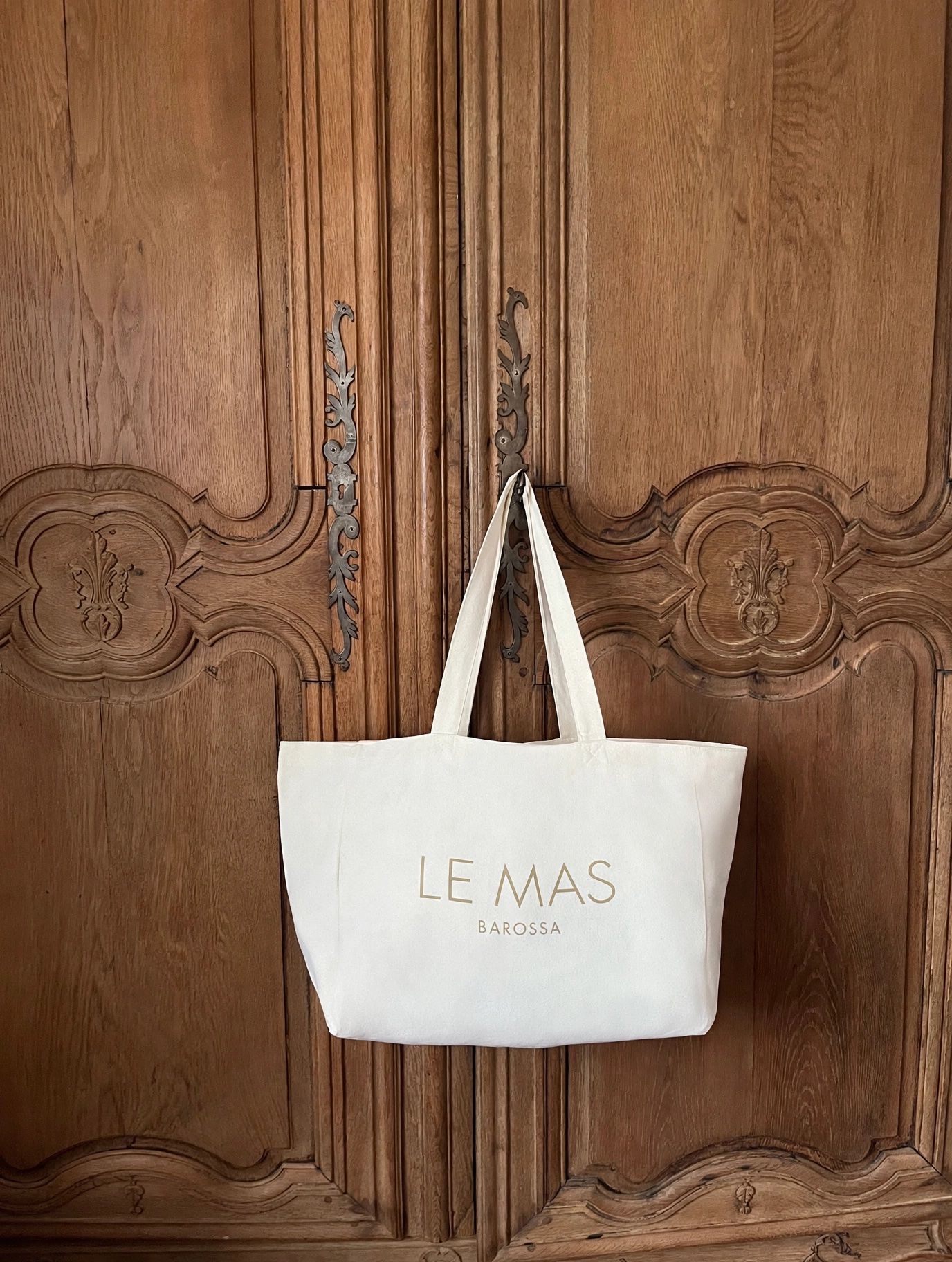 A white tote bag hanging on a wooden door with carved designs.