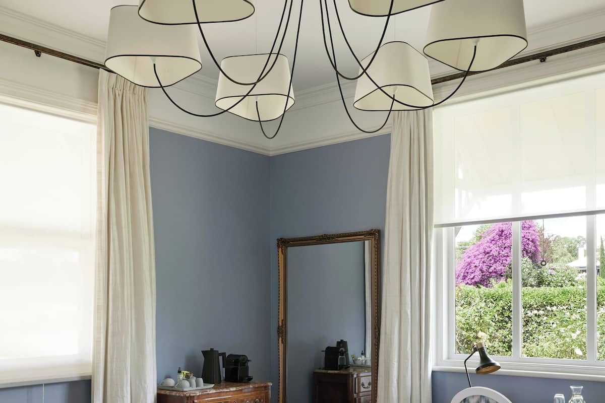 Un dormitorio con cama, cómoda, escritorio con silla, espejo grande y ventana con cortinas.