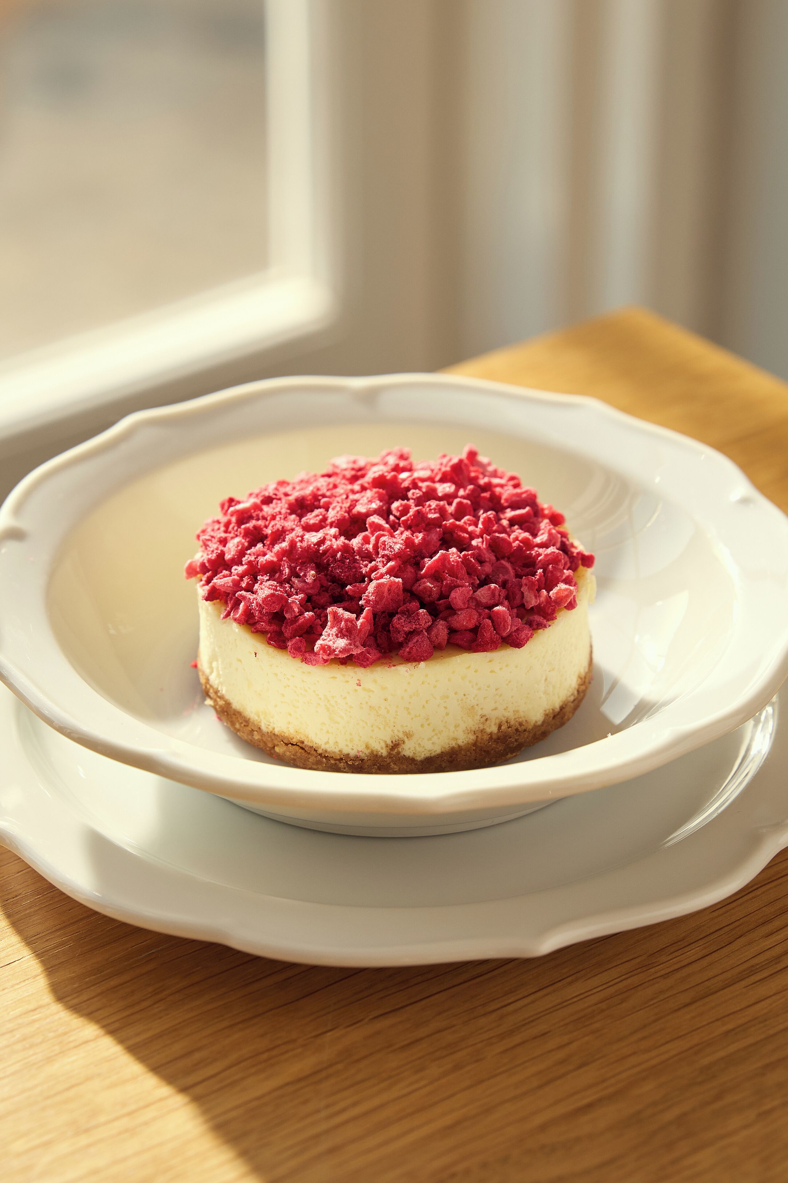 A cheesecake on a white plate with a decorative edge, placed on a wooden table.