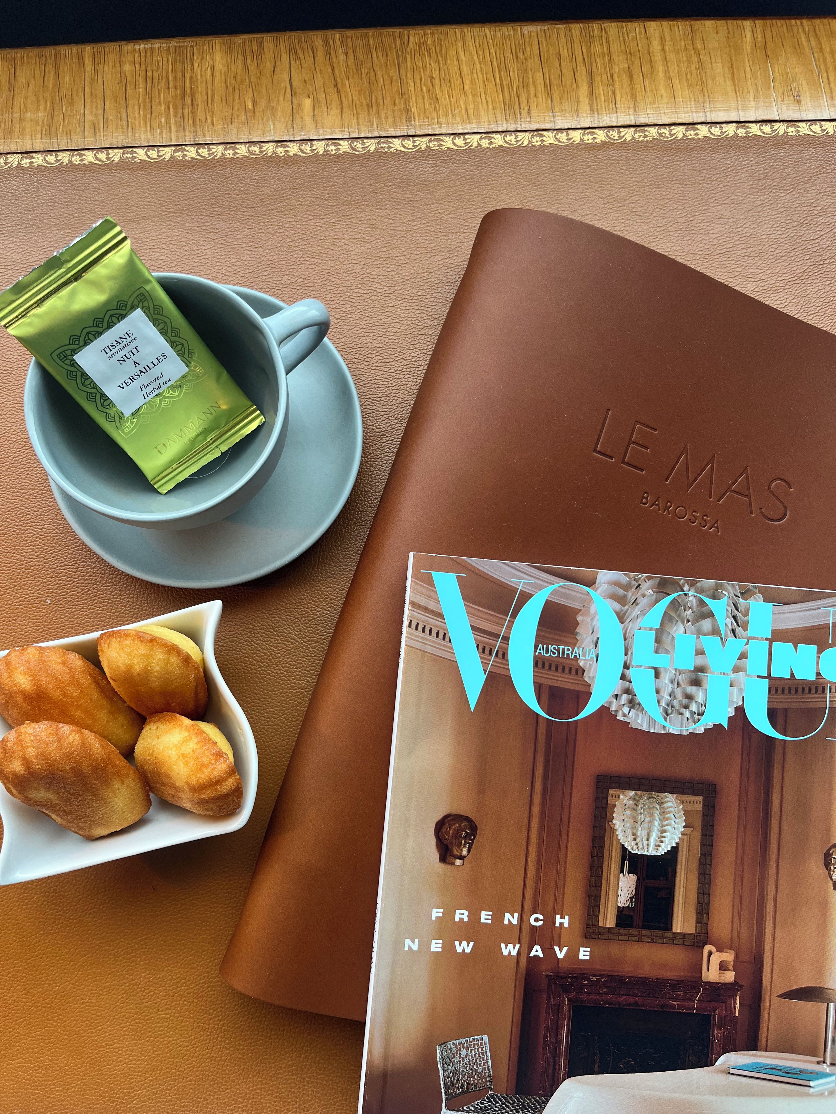 En bog i læderindbinding med titlen 'Vogue Australia French New Wave' og en kop med en grøn tebrev på et bord.