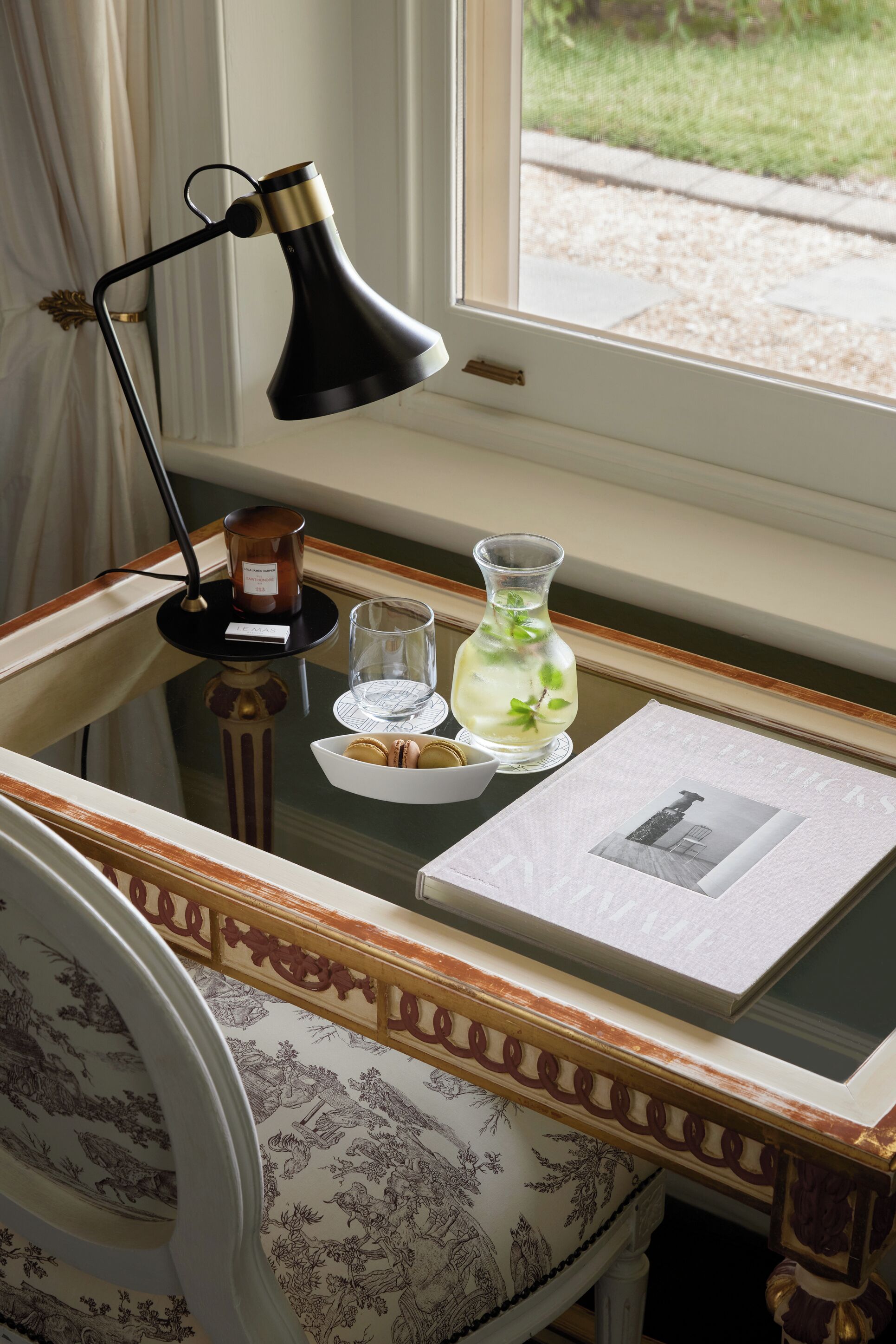 A desk with a lamp, a vase, a glass, and a framed picture.