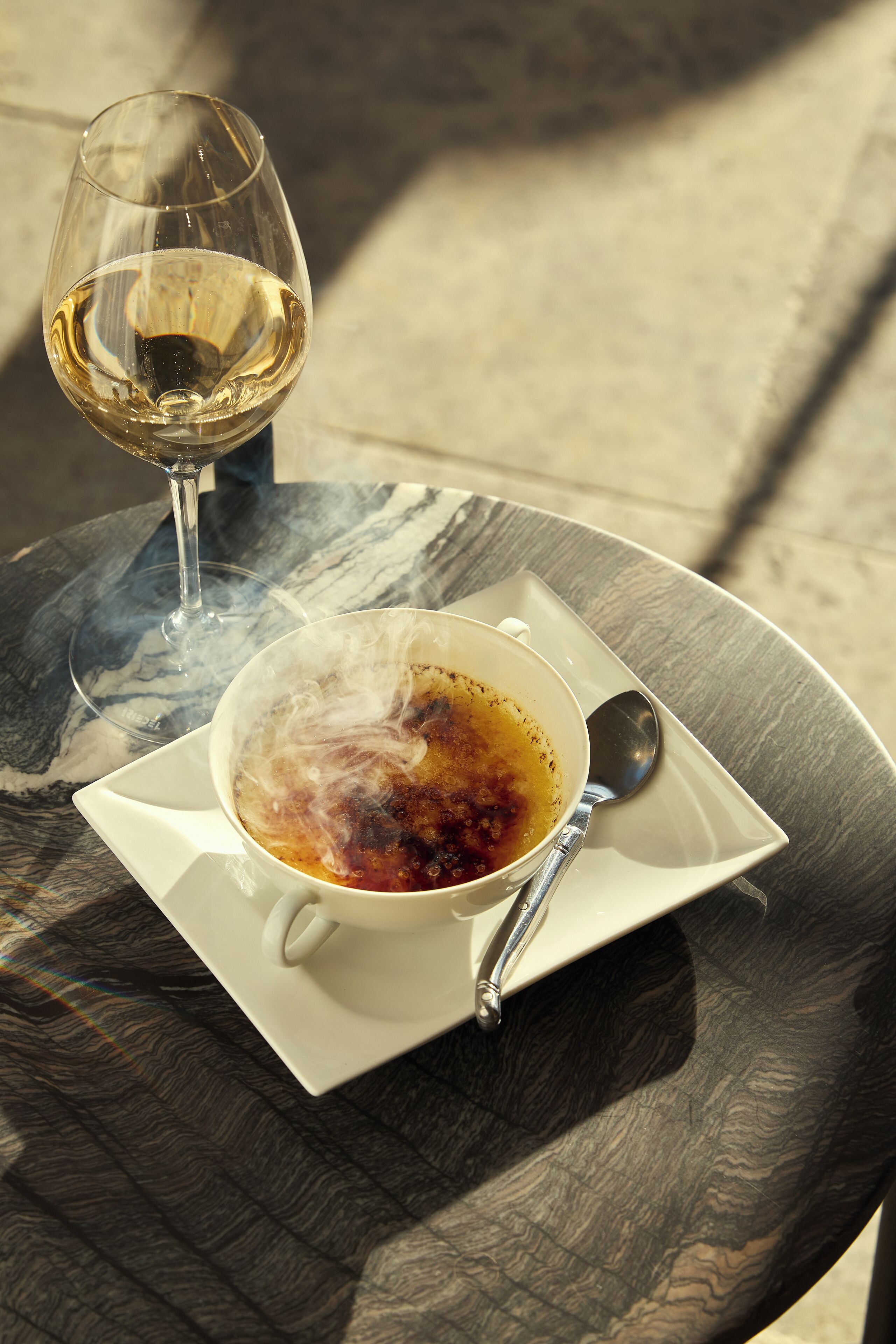 A table with a glass of white wine and a cup of coffee with steam, on a marble table.